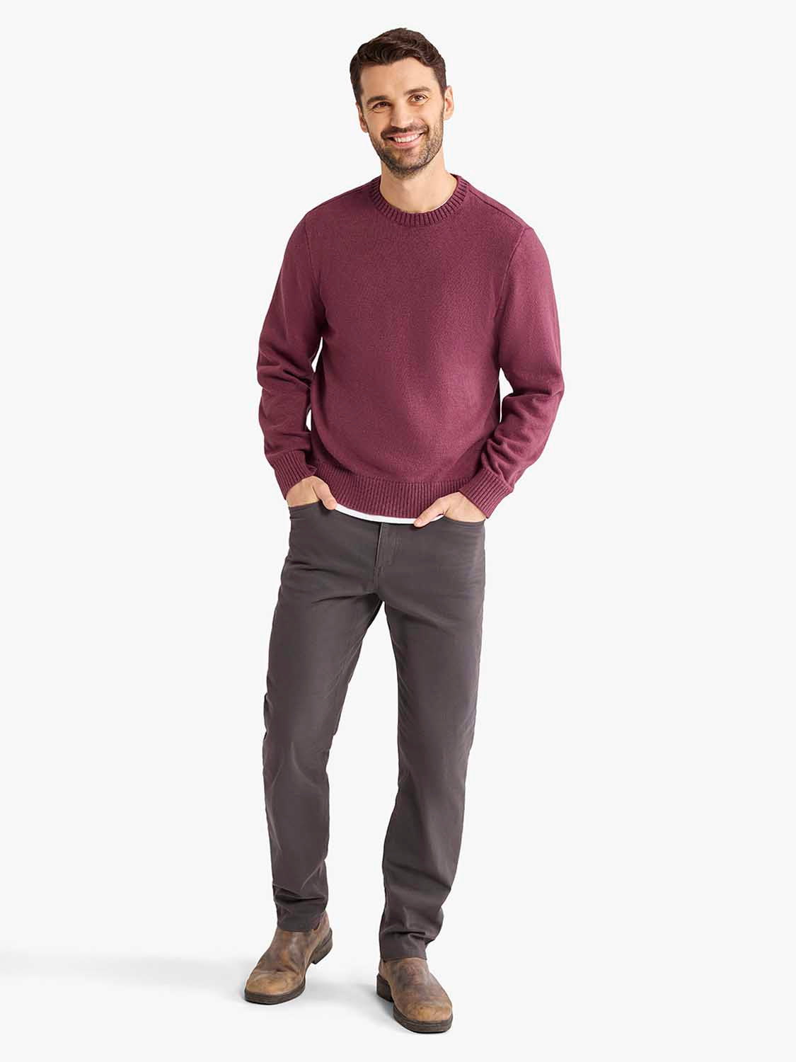 Man wearing a burgundy crew neck sweater with ribbed trim and gray pants.