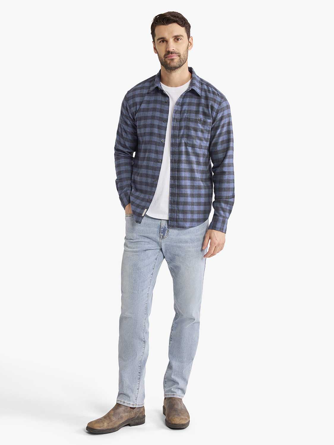 Man wearing a blue checked flannel shirt over a white tee, paired with light-wash jeans and brown suede boots.