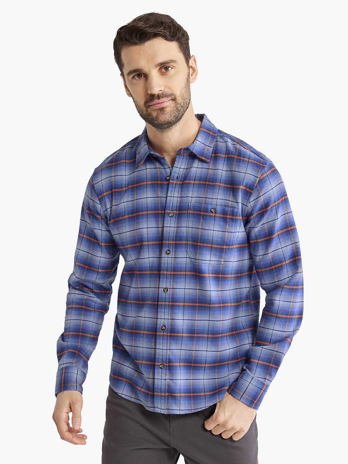 Man wearing a blue plaid flannel shirt with orange and white stripes over gray pants.
