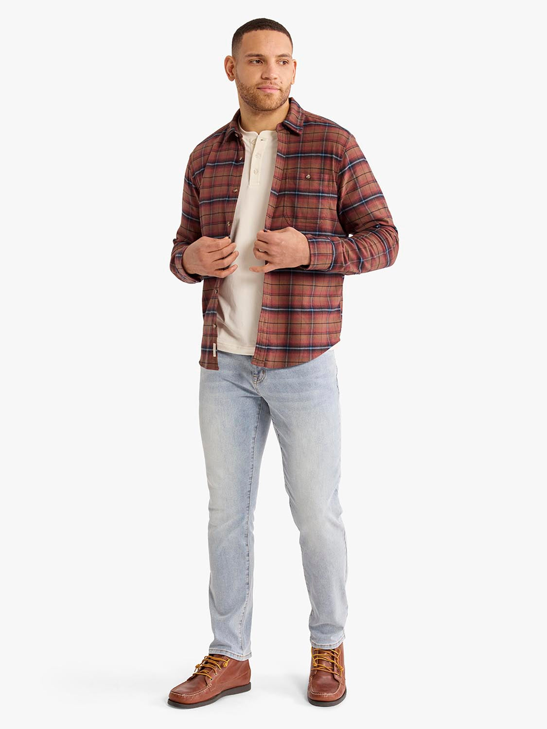 Man wearing a burgundy plaid flannel shirt over a cream-colored shirt with light blue jeans.
