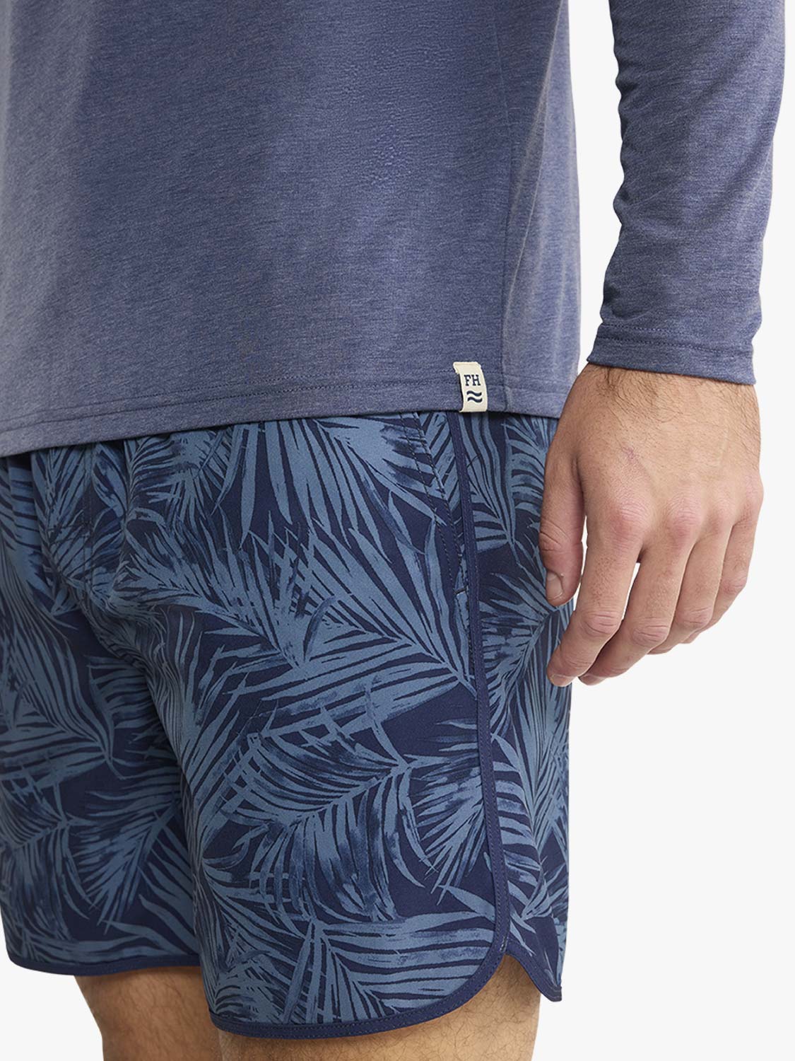 Navy hoodie with long sleeves worn over patterned swim shorts with tropical leaf design.