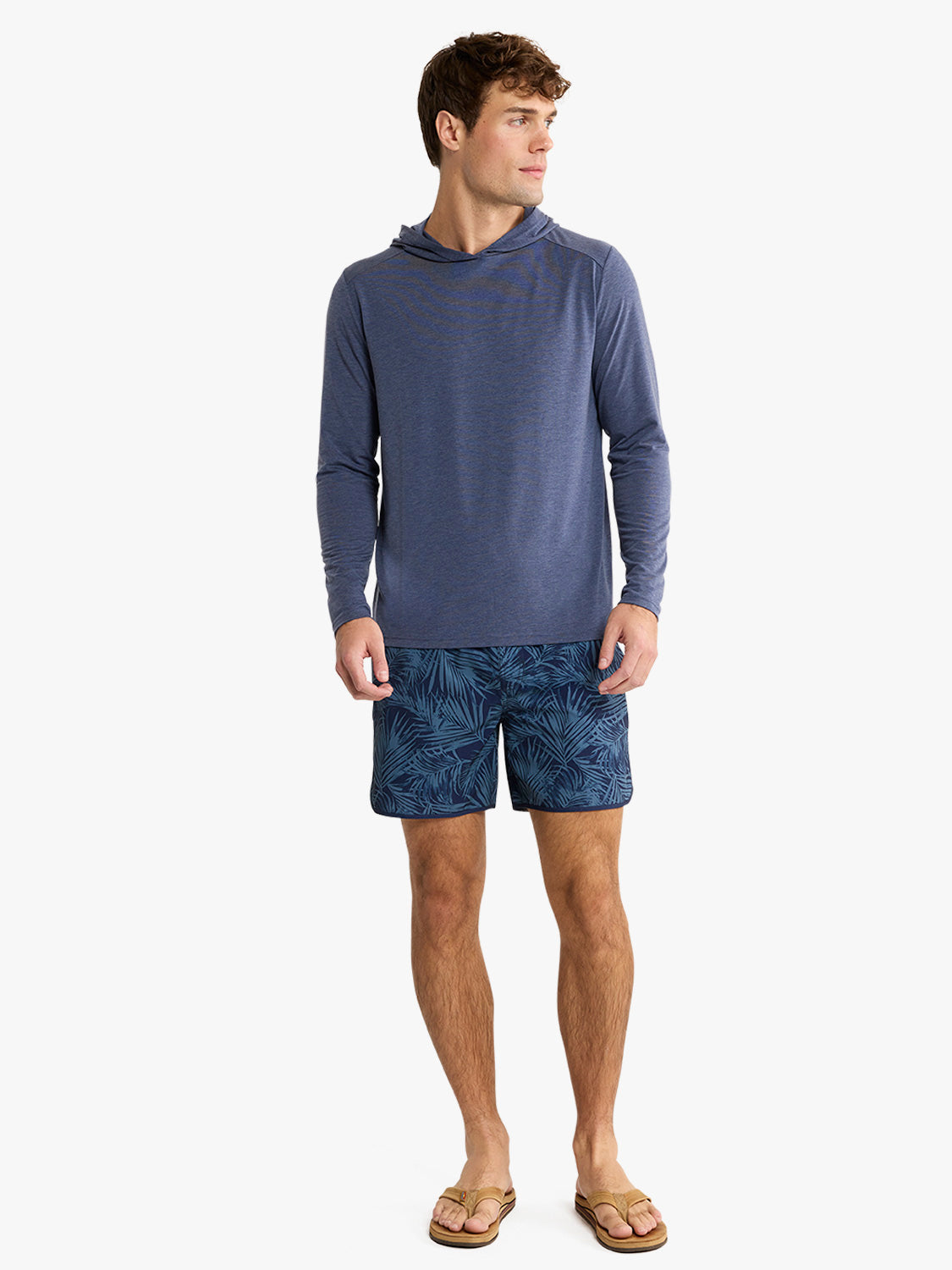 Man wearing a navy blue hoodie with long sleeves and patterned navy shorts.