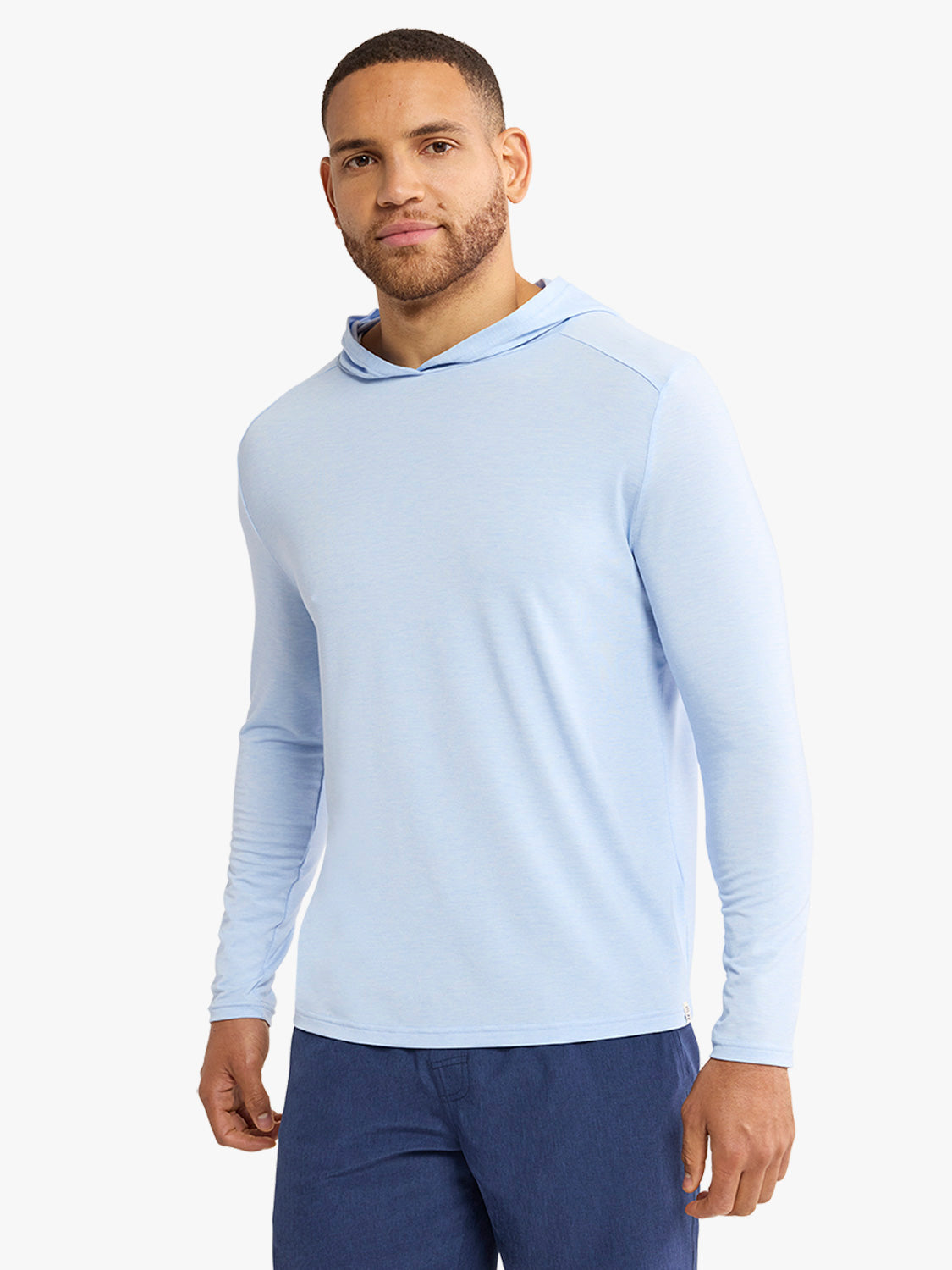 Man wearing a light blue hoodie with long sleeves and a drawstring hood paired with dark navy pants.