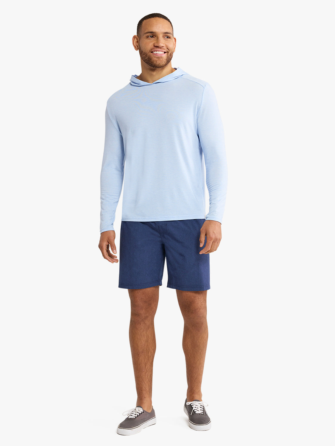 Man wearing a light blue hooded long-sleeve hoodie and navy shorts with gray sneakers.