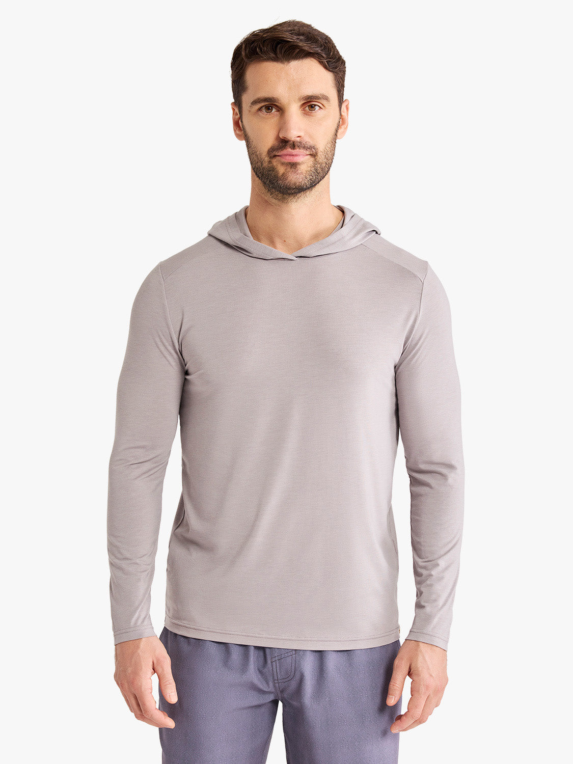 Man wearing a light gray hooded long-sleeve shirt with blue pants against a white background.