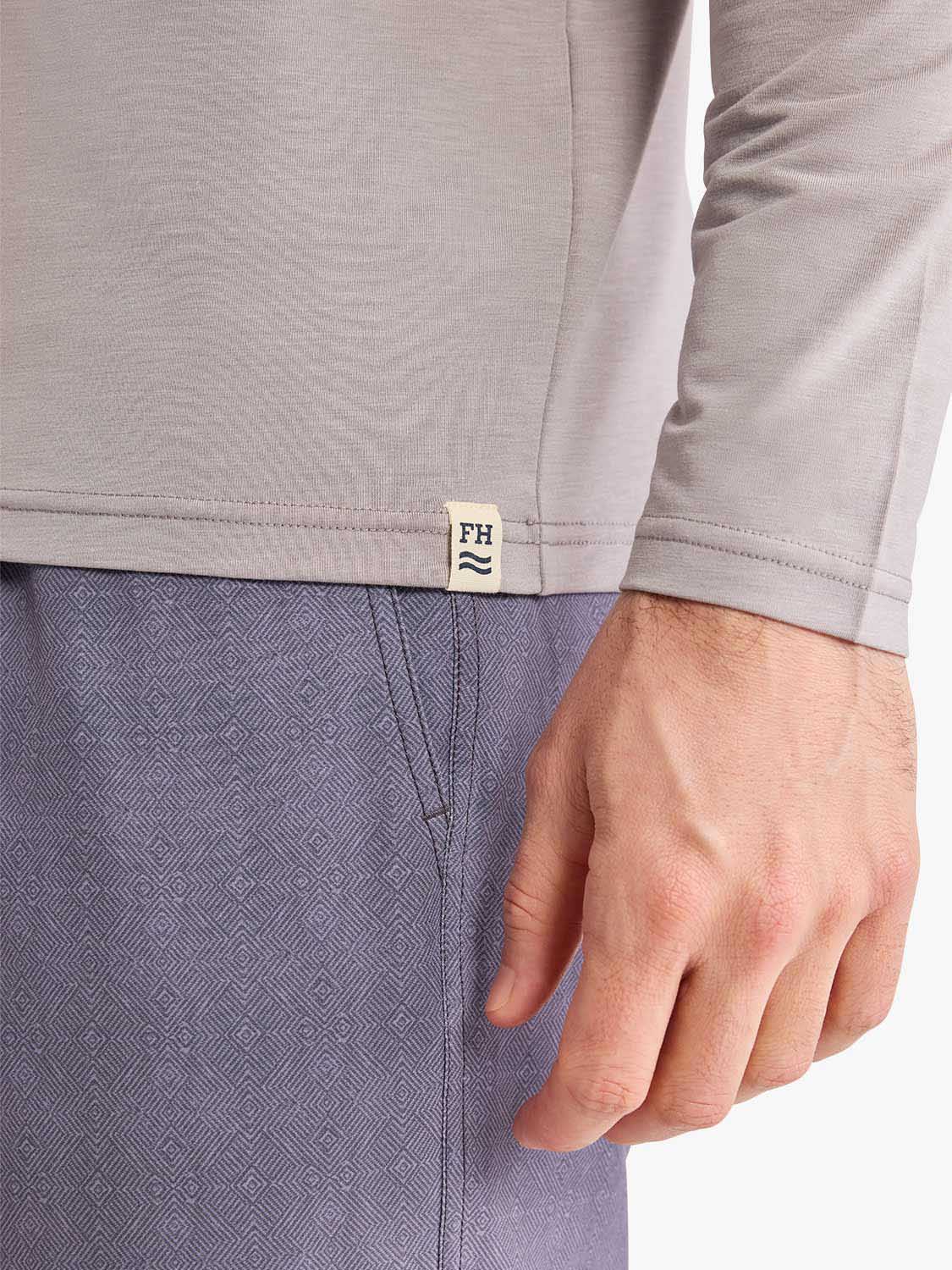 Beige hoodie with branded label worn over patterned blue shorts on a person.