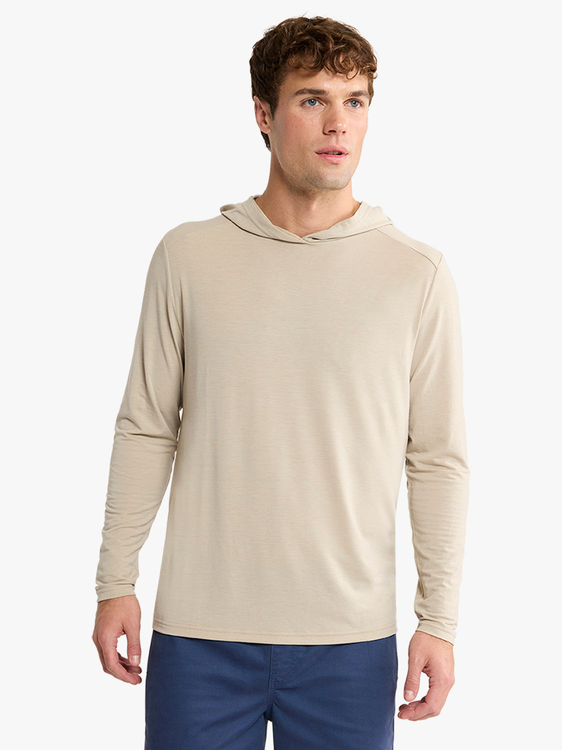 Man wearing a sand-colored long-sleeve hoodie with navy blue pants against a white background.