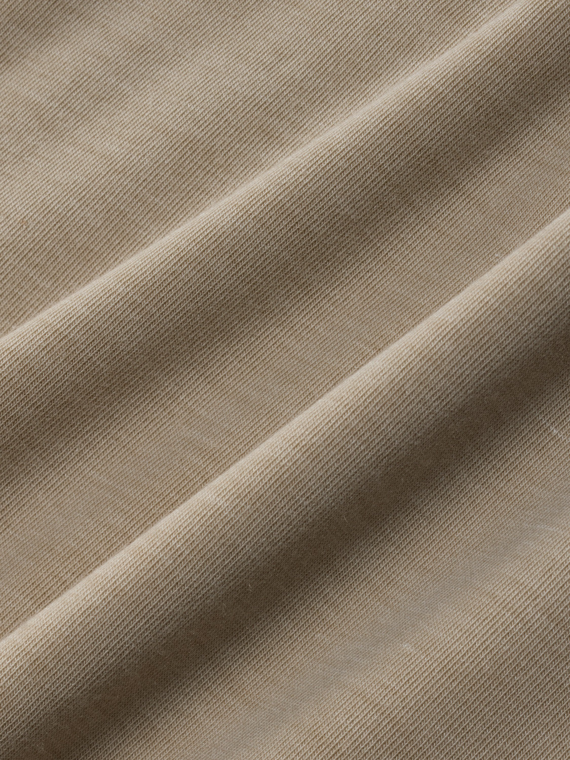 Close-up of sand-colored knit fabric showing textured ribbed surface with natural folds and shadows.