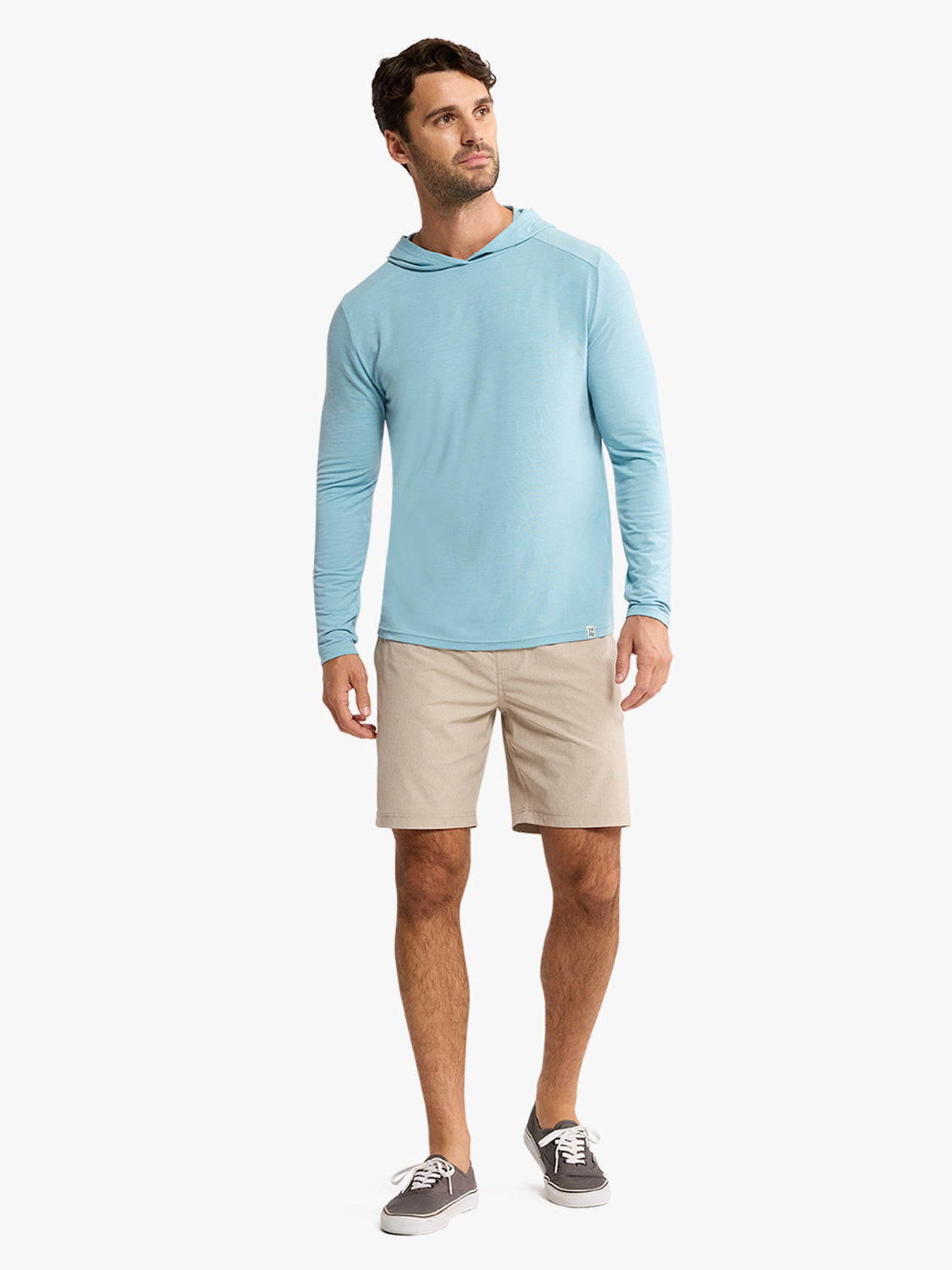 Man wearing a bay blue long-sleeve hoodie with khaki shorts and gray canvas sneakers.