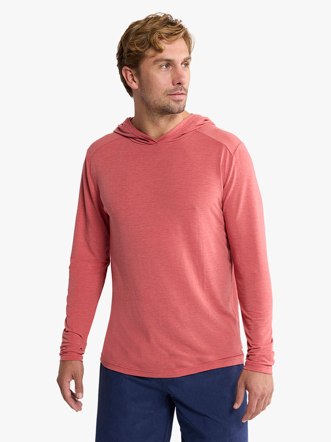 Man wearing a mineral red long-sleeve hoodie with a textured fabric finish and navy pants.