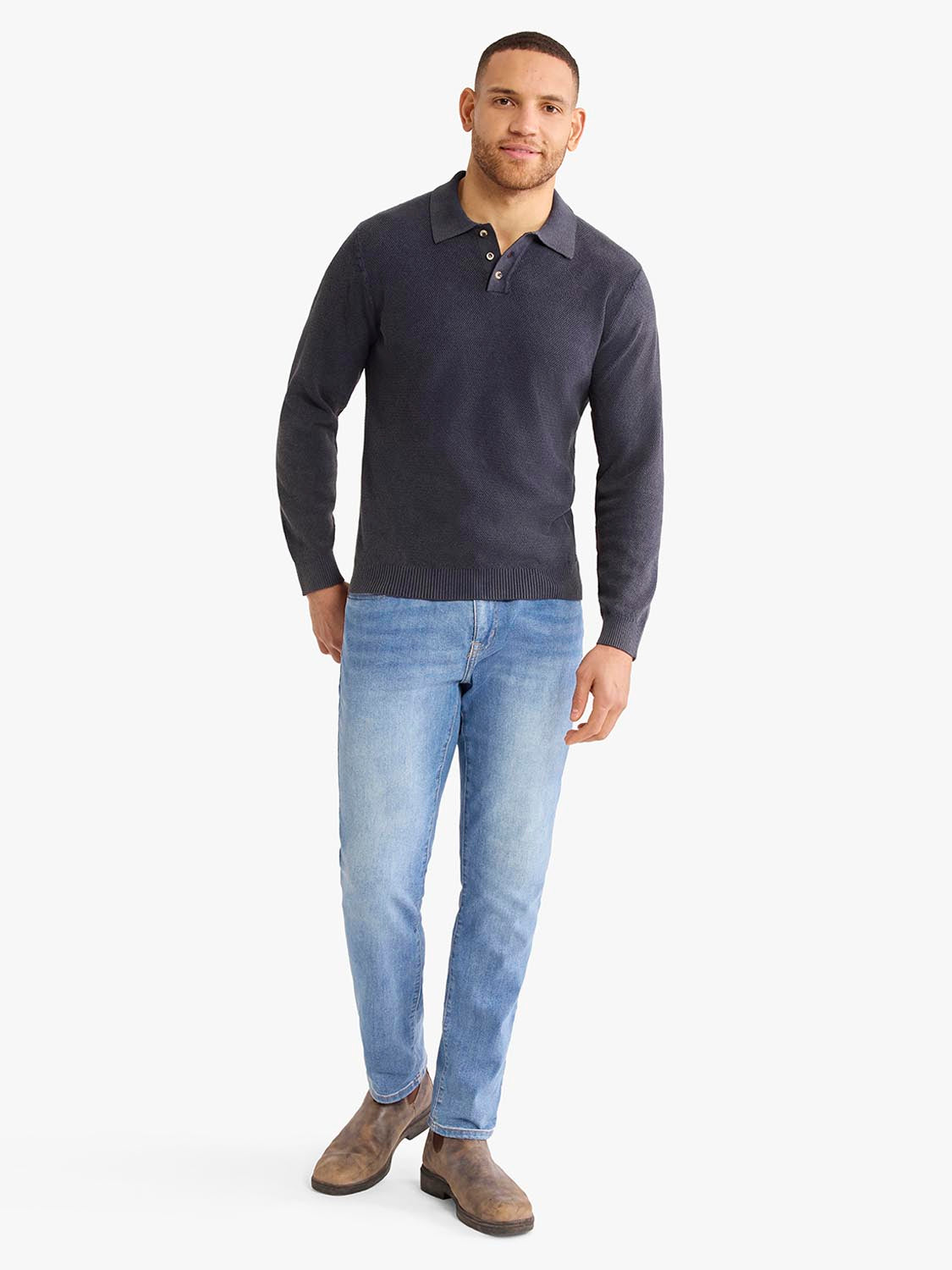 Man wearing a navy long sleeve polo shirt with light blue jeans and brown boots.