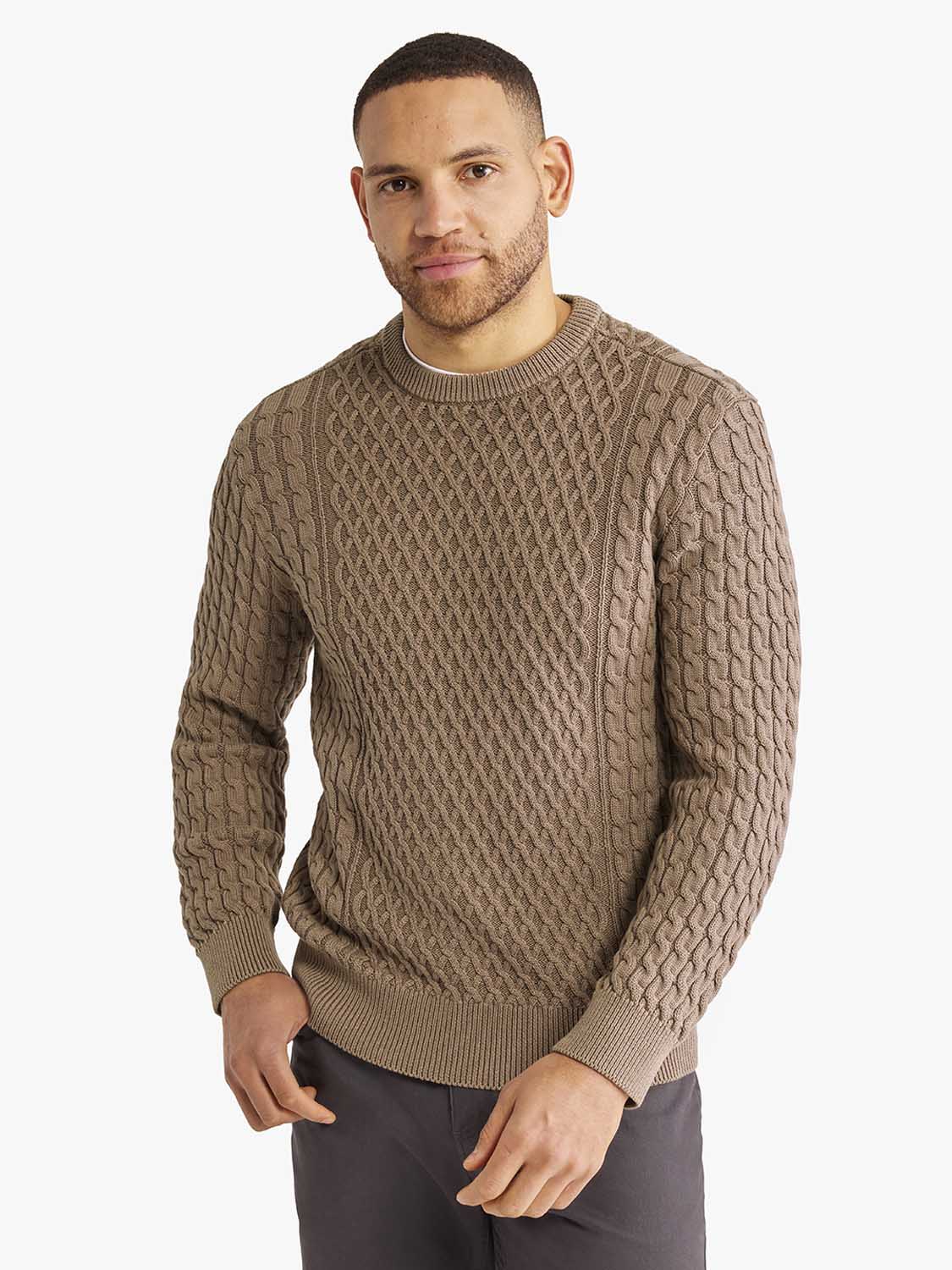 Man wearing a tan cable knit sweater with a crew neckline and ribbed cuffs.