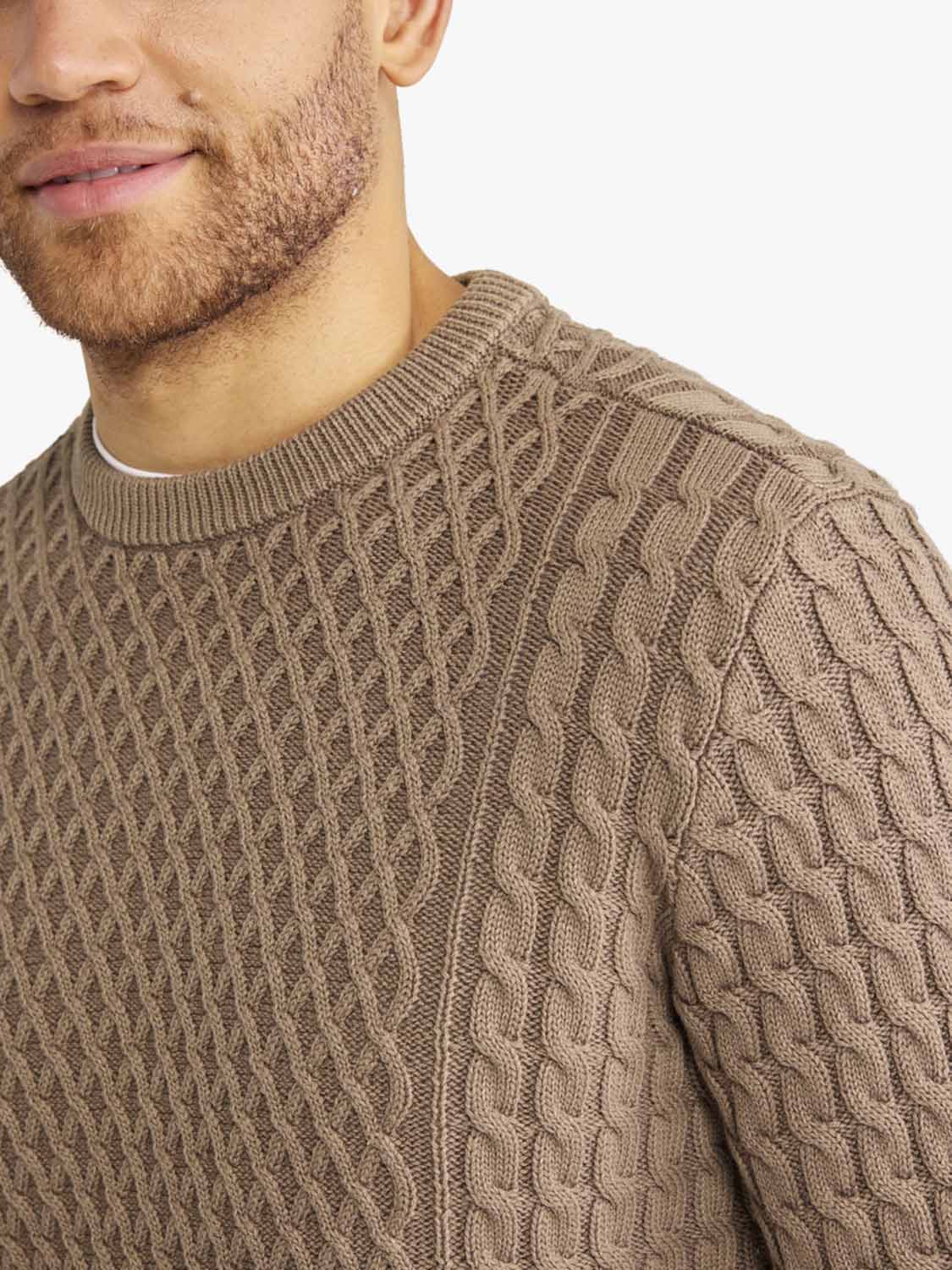 Man wearing a tan cable knit sweater with a crew neckline and textured pattern.