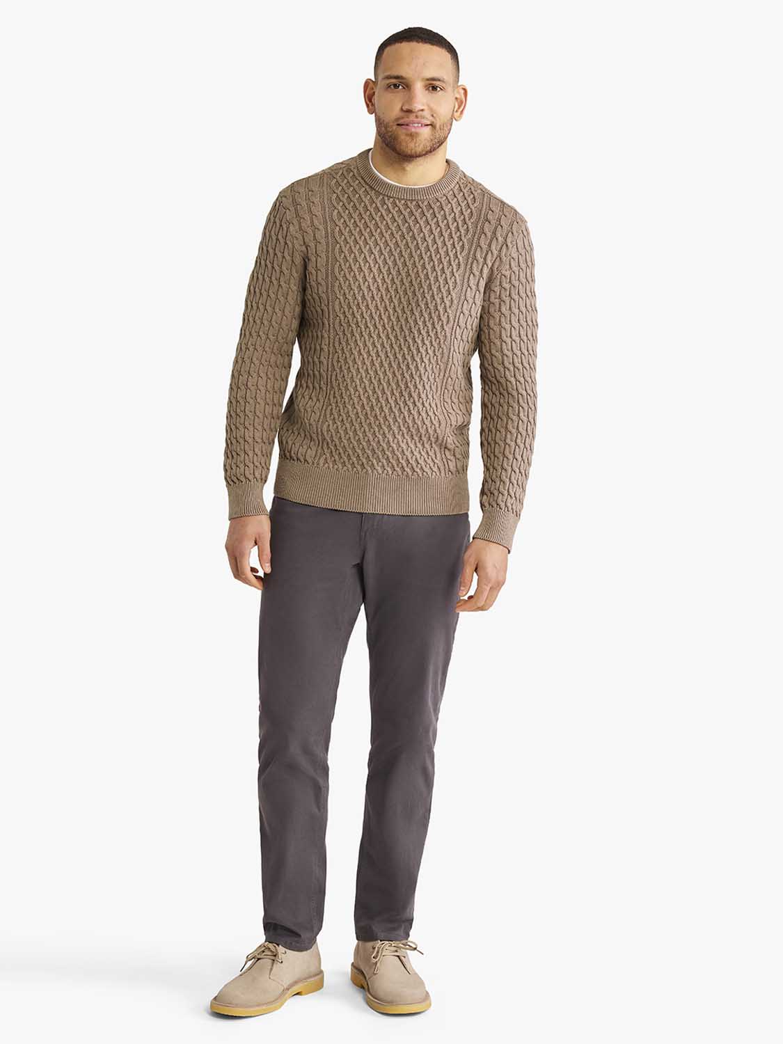 Man wearing an oak-colored cable knit crew neck sweater with dark gray pants and beige desert boots.