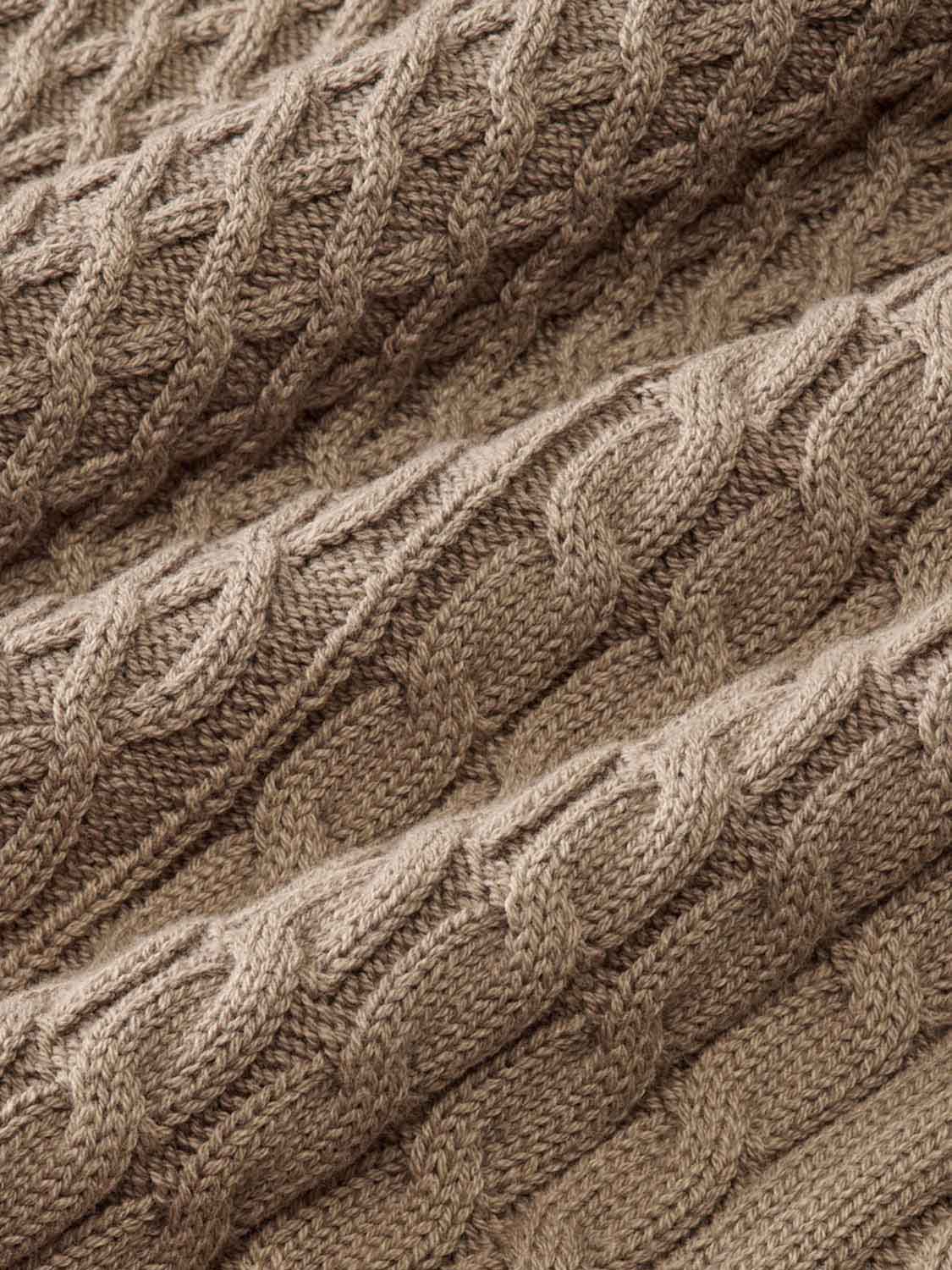 Close-up of tan cable knit sweater texture showing diagonal twisted stitch pattern detail.