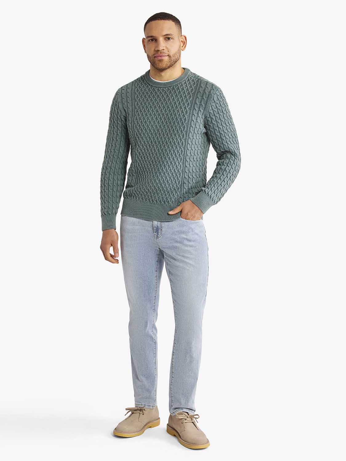 Man wearing a seagreen cable knit sweater with light blue jeans and tan boots.