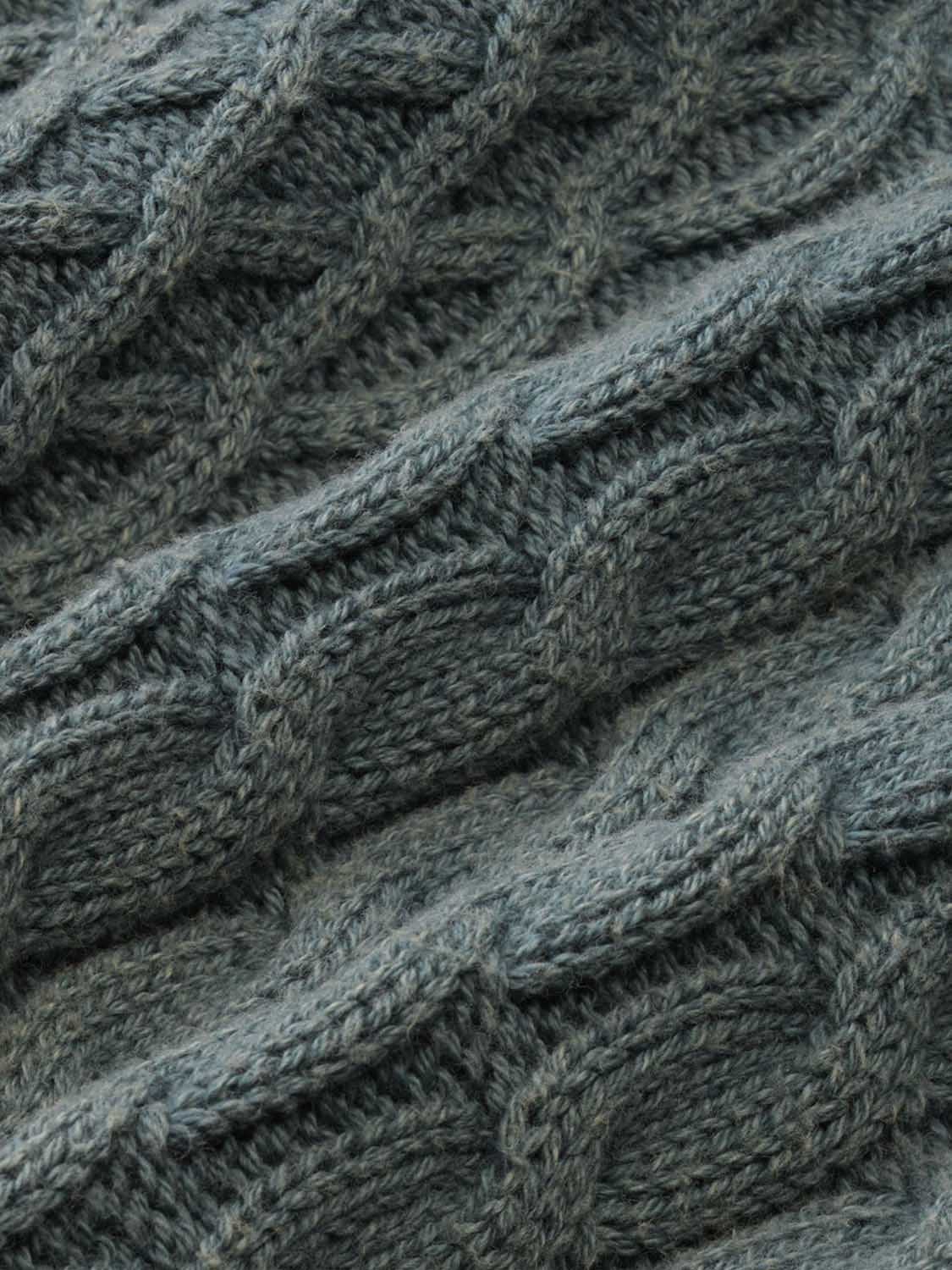 Close-up of seapine green cable knit sweater texture showing diagonal woven pattern details.