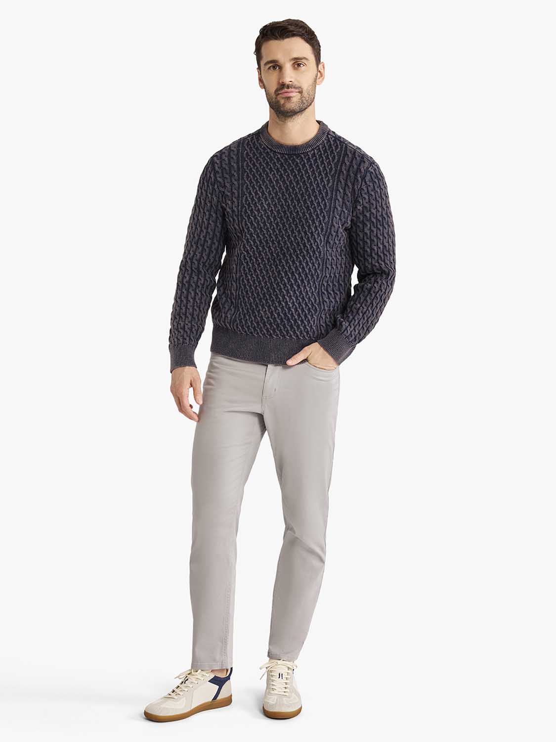 Man wearing a navy cable knit sweater with gray pants and cream sneakers.