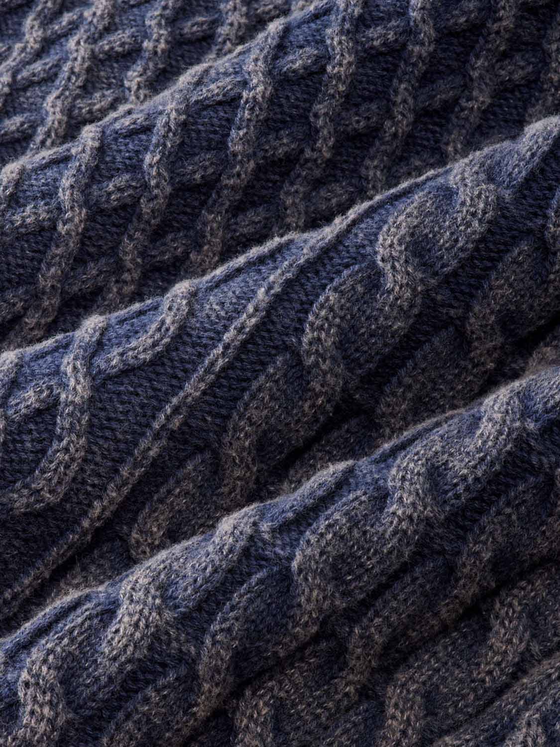 Close-up of navy cable knit sweater texture showing raised twisted pattern and knitted fibers.