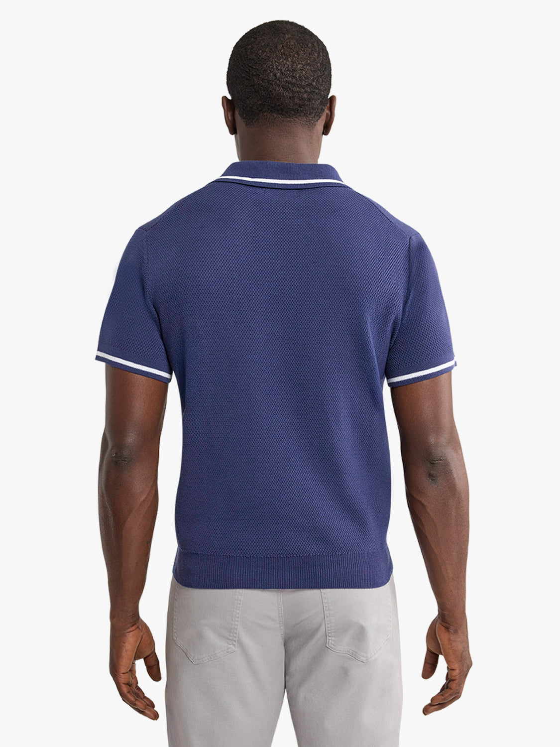 Man wearing a navy short-sleeve sweater polo with white trim and light gray pants.