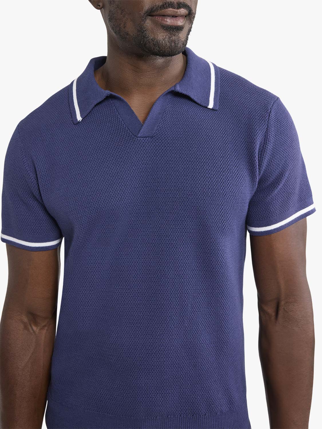 Man wearing a navy sweater polo with white stripe trim on the collar and sleeves.
