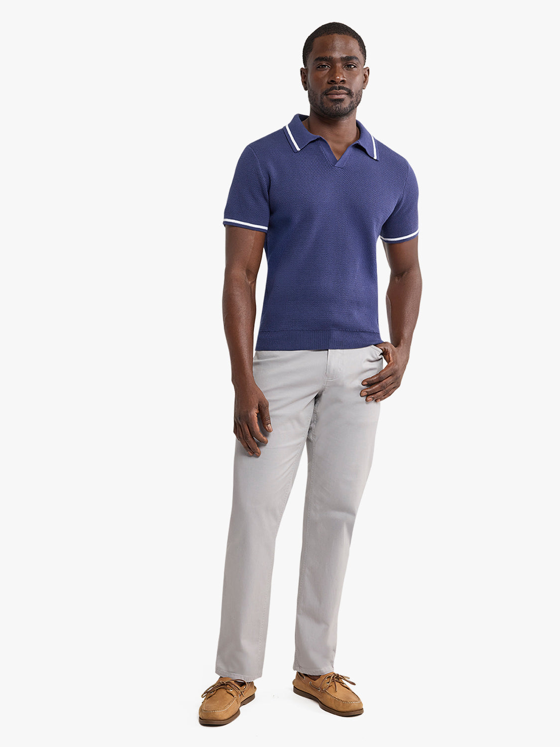 Man wearing a navy sweater polo with white-tipped collar and sleeves, paired with light gray pants.