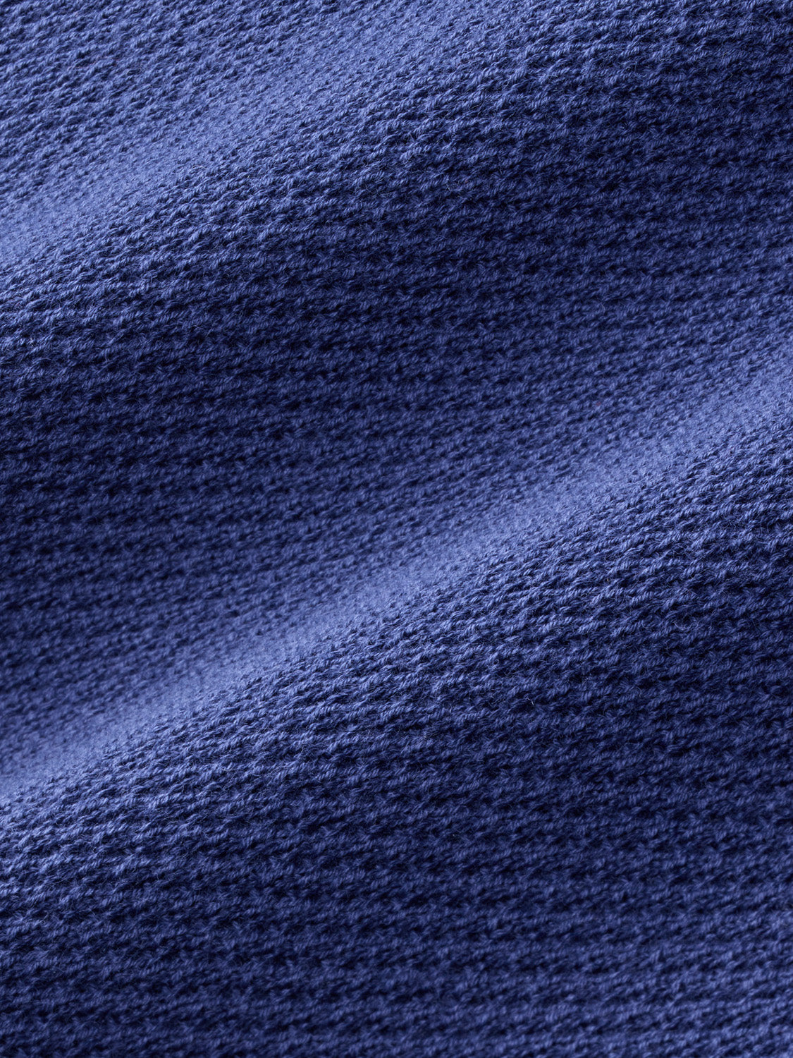 Close-up of navy knit fabric texture with diagonal ribbed pattern and subtle color variation.