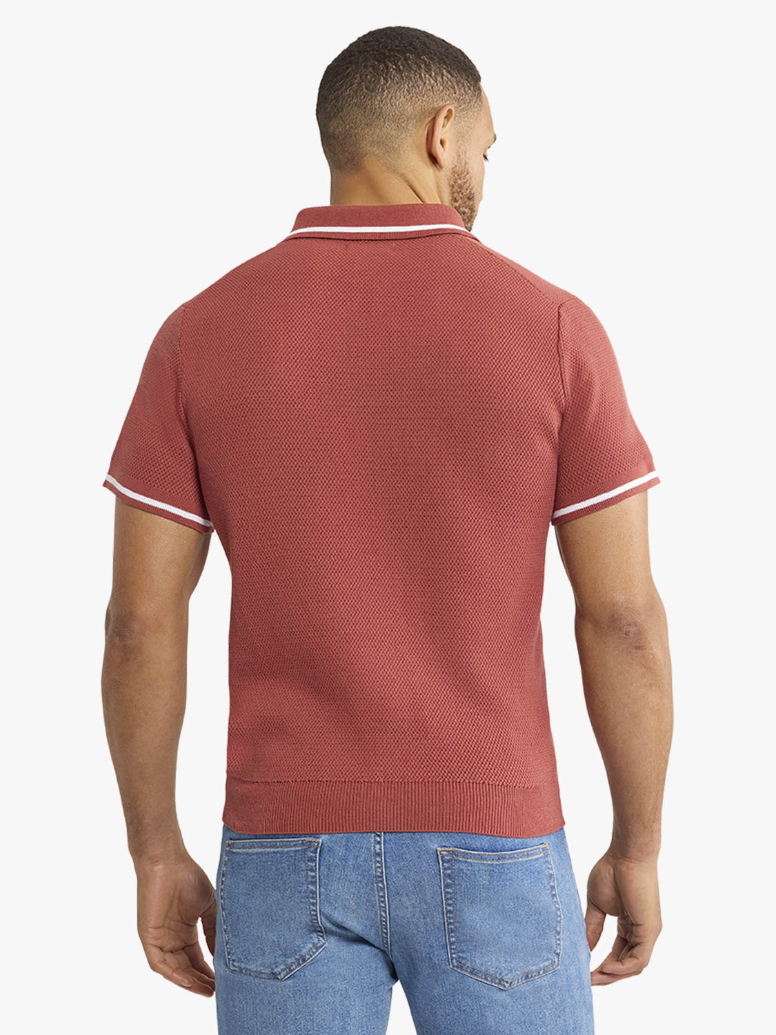 Man wearing a washed red short-sleeve sweater polo with white striped trim and blue jeans.