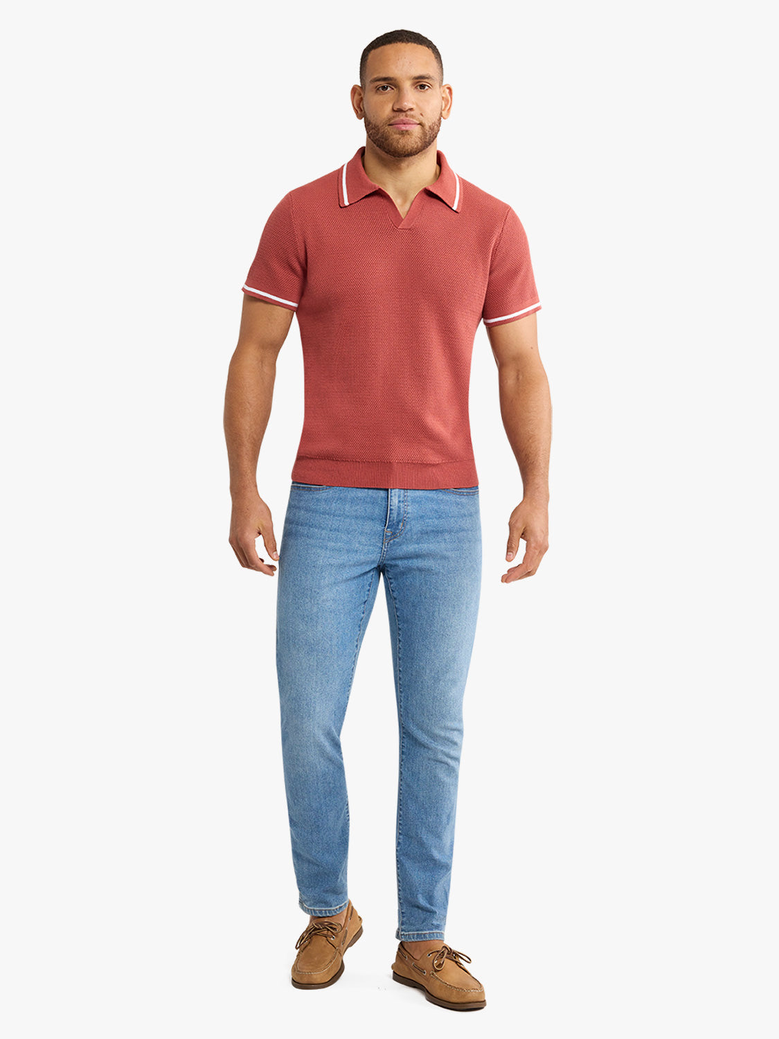 Man wearing washed red short-sleeve polo sweater with white trim and blue jeans.