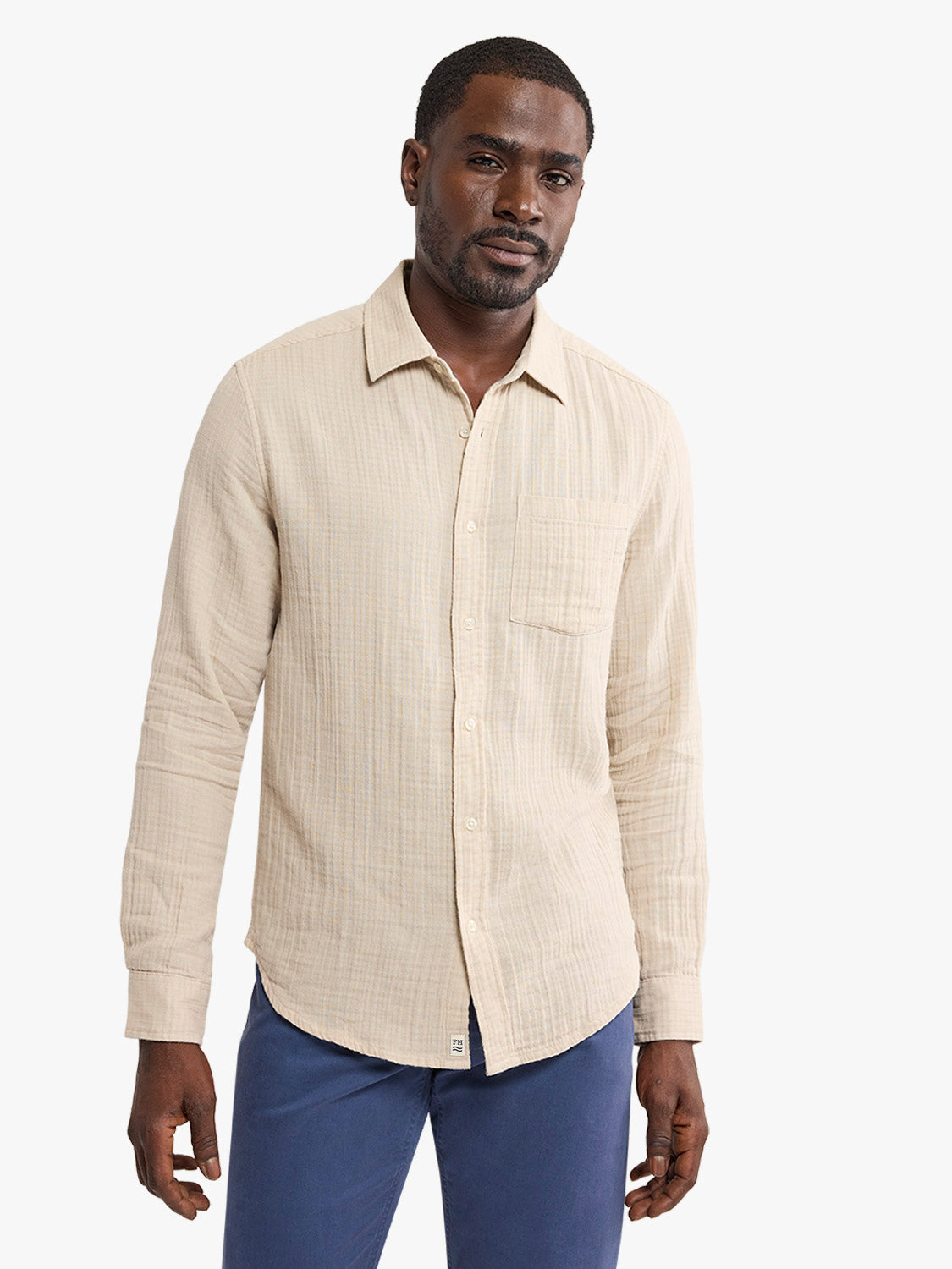 Man wearing a cream-colored long-sleeve button-up shirt with vertical stripes and navy trousers.