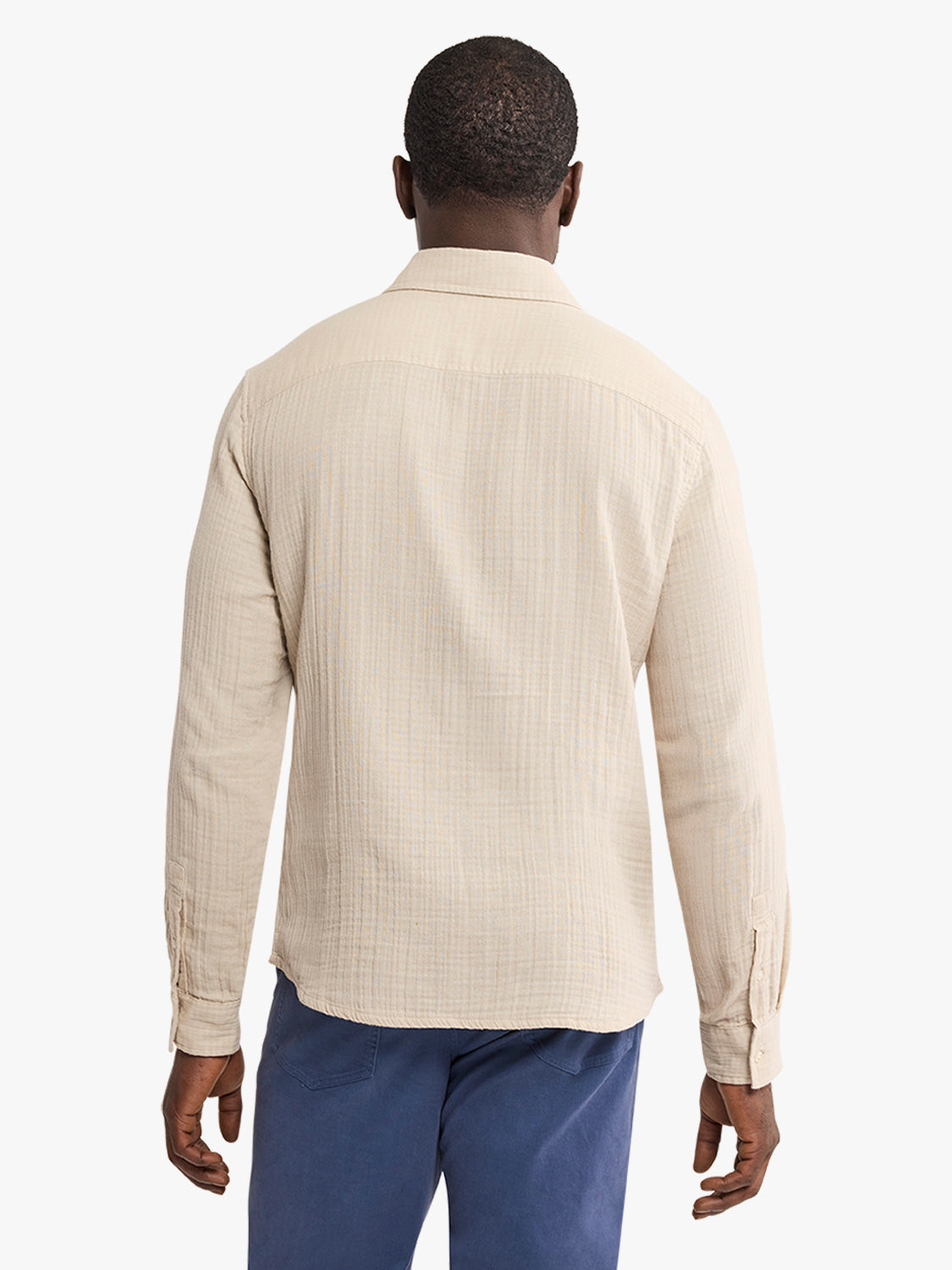 Man wearing a cream-colored textured button-up shirt with long sleeves and navy pants.