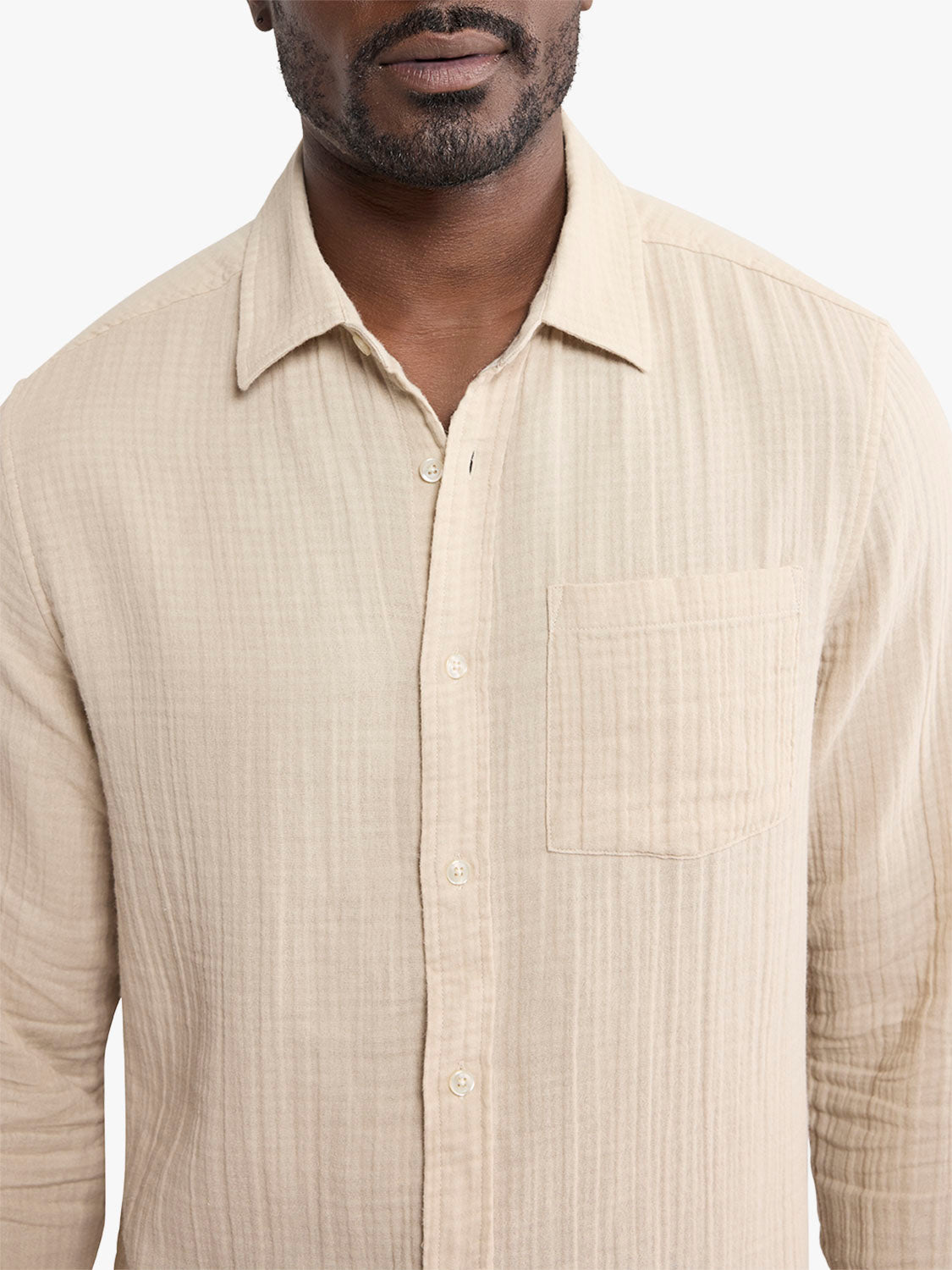 Man wearing a beige textured button-up shirt with a chest pocket and long sleeves.