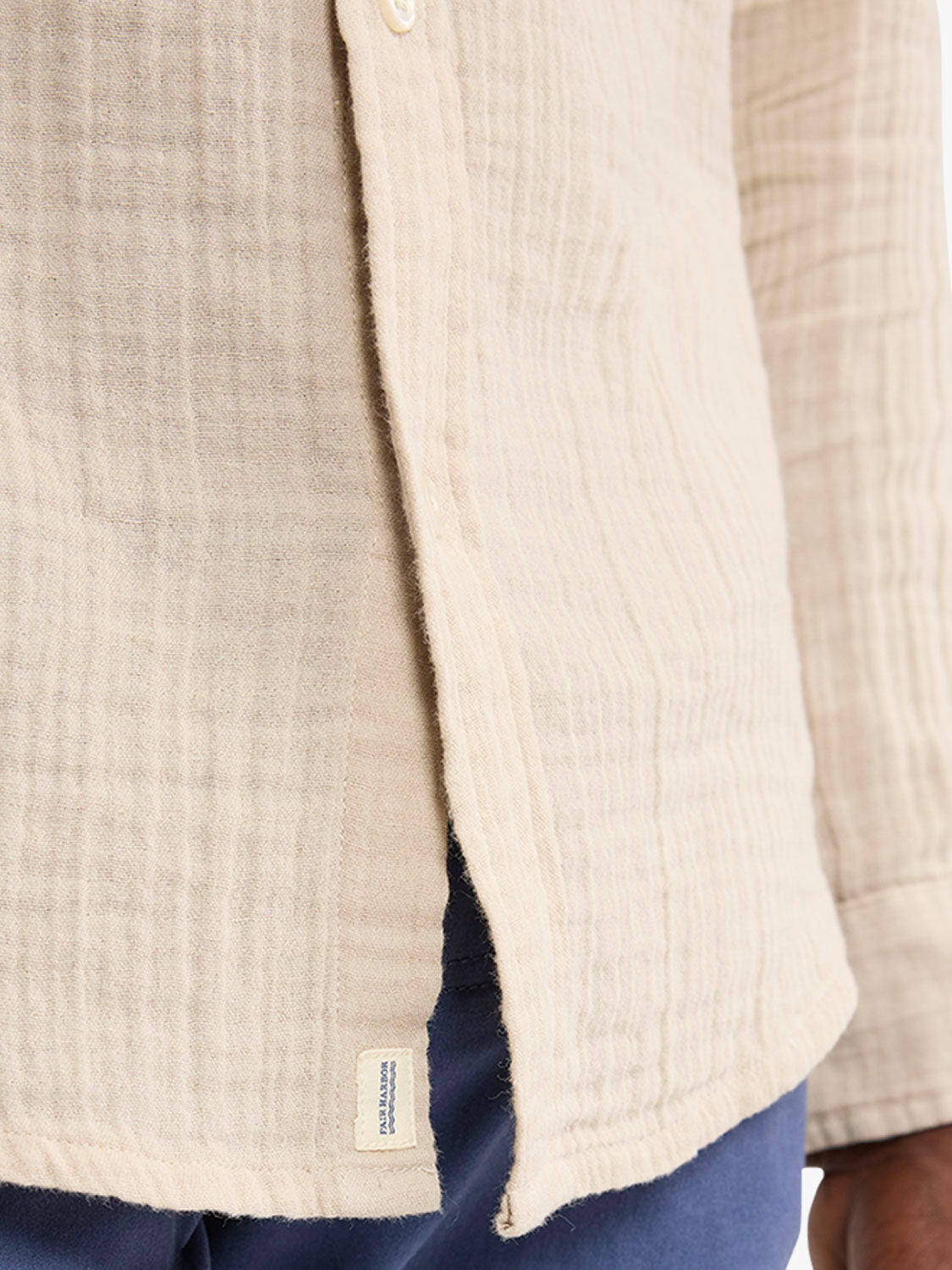 Cream linen button-up shirt with vertical texture, shown from side detail with navy pants visible beneath.