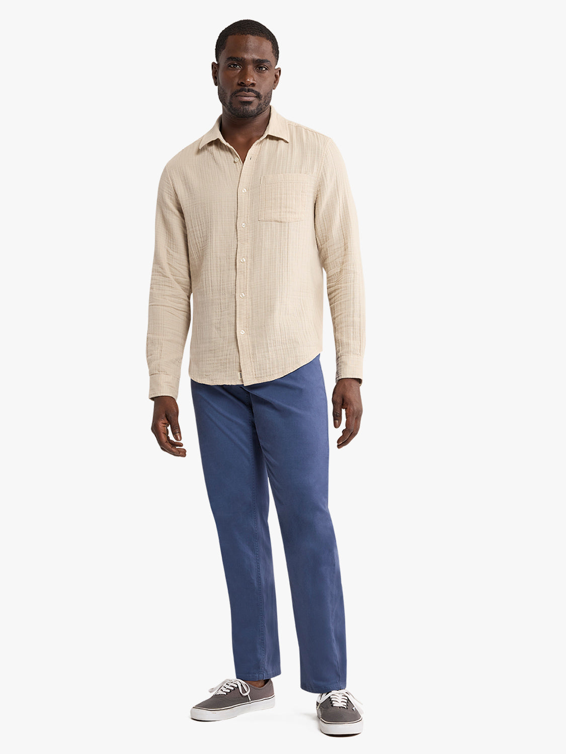 Man wearing a cream-colored textured button-up shirt with blue jeans and gray sneakers.