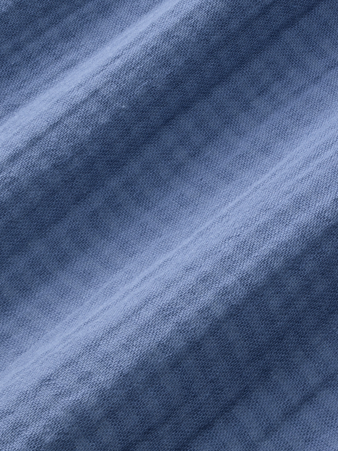 Blue textured fabric with a diagonal weave pattern and natural folds throughout the material.