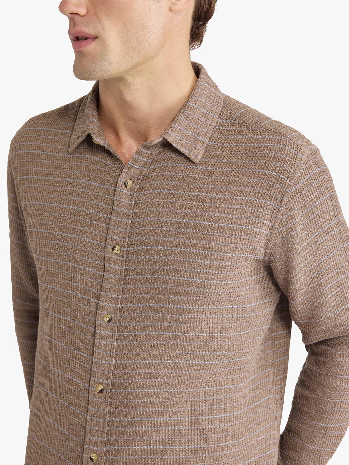 Man wearing a long-sleeve button-up shirt with horizontal tan and white striped waffle texture pattern.