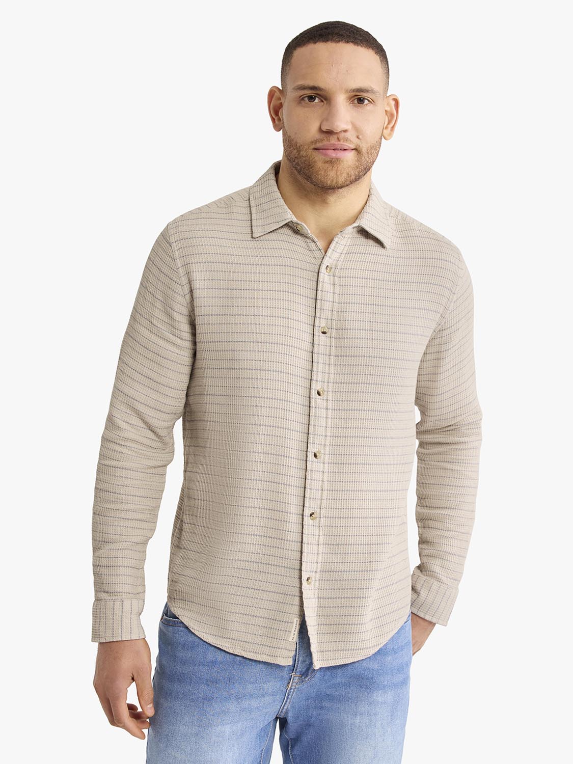 Man wearing a beige long sleeve button-up shirt with horizontal waffle stripe texture and blue jeans.