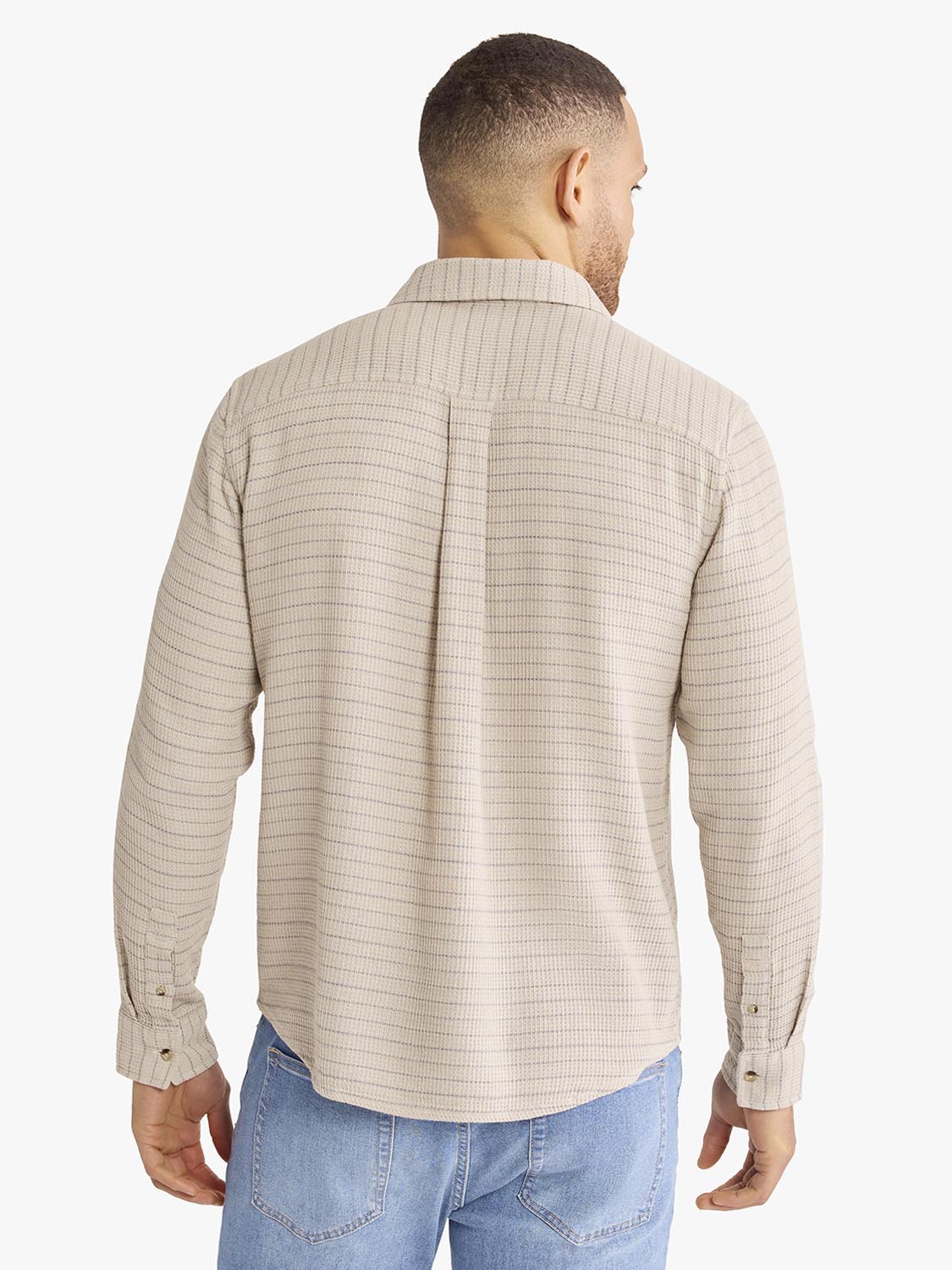 Man wearing beige waffle stripe long sleeve button-up shirt with blue jeans, shown from back view.