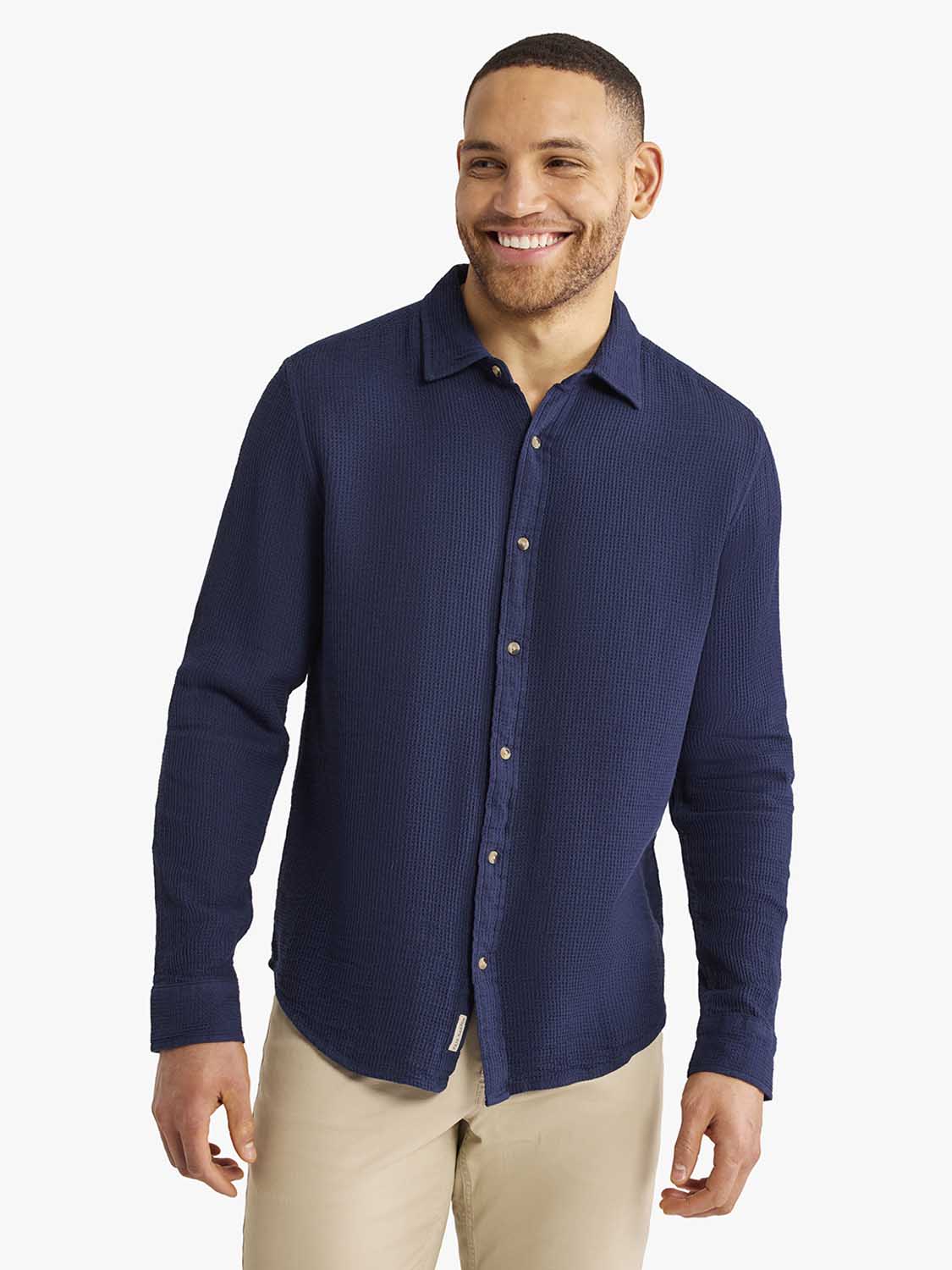 Man wearing a navy waffle-textured long sleeve button-up shirt with a collared neckline.