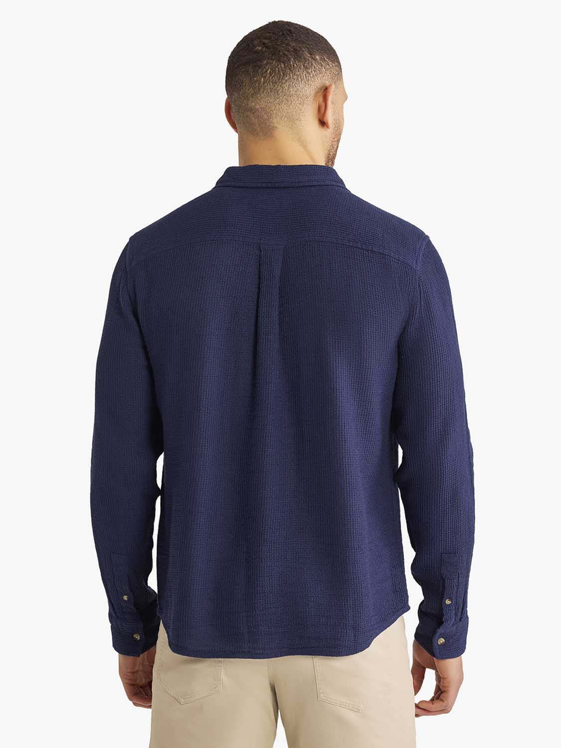 Man wearing navy waffle-textured long sleeve button-up shirt, shown from back view.
