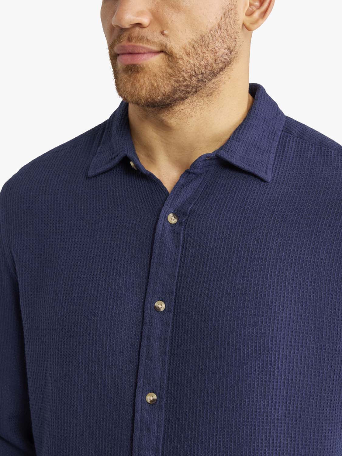 Man wearing a navy waffle-textured long sleeve button-up shirt with gold buttons.