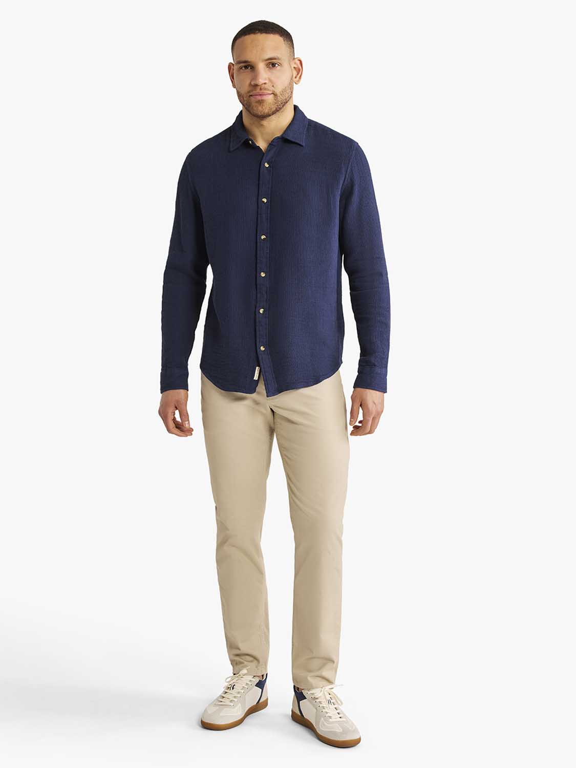 Man wearing a navy waffle-textured long sleeve button-up shirt paired with beige trousers.