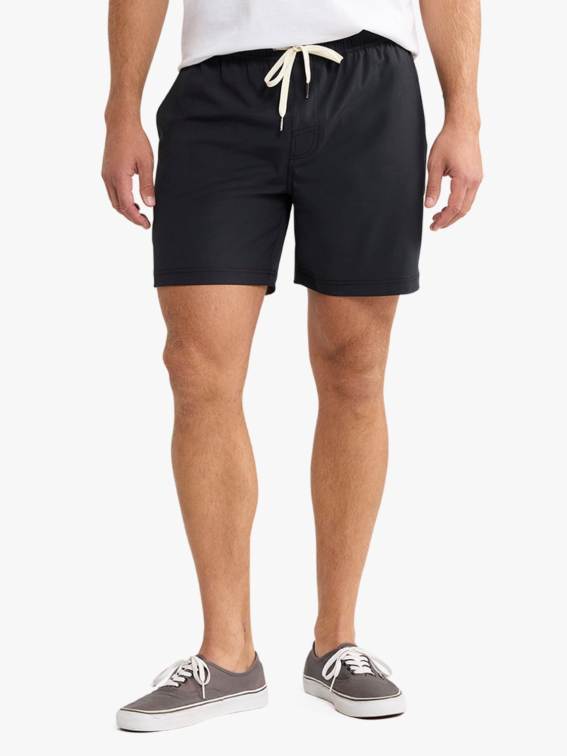 Man wearing black shorts with cream drawstring waist and gray canvas sneakers.