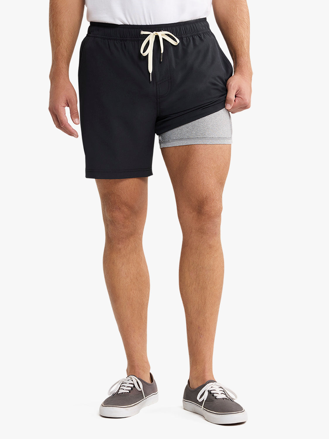 Man wearing black shorts with gray liner shorts and a cream drawstring, paired with gray canvas sneakers.