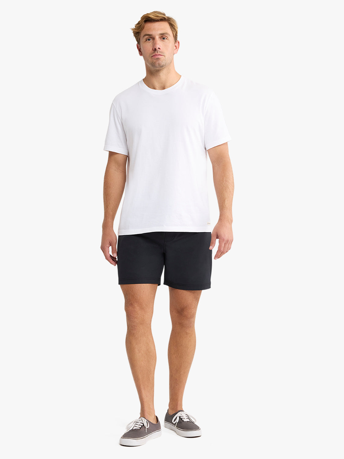 Man wearing a white crew-neck t-shirt and black shorts standing against a white background.