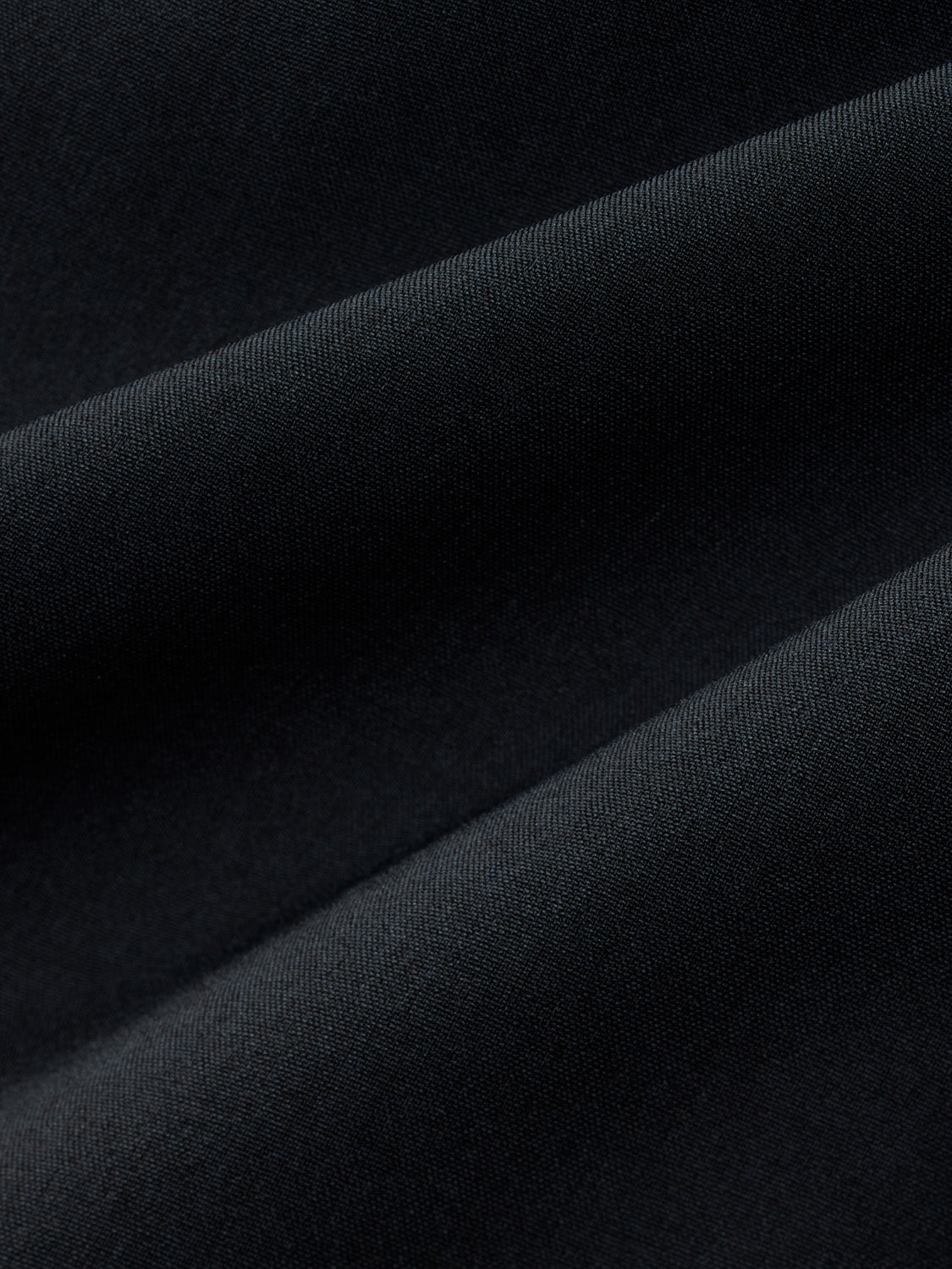 Close-up of black fabric with diagonal folds and textured weave pattern throughout.