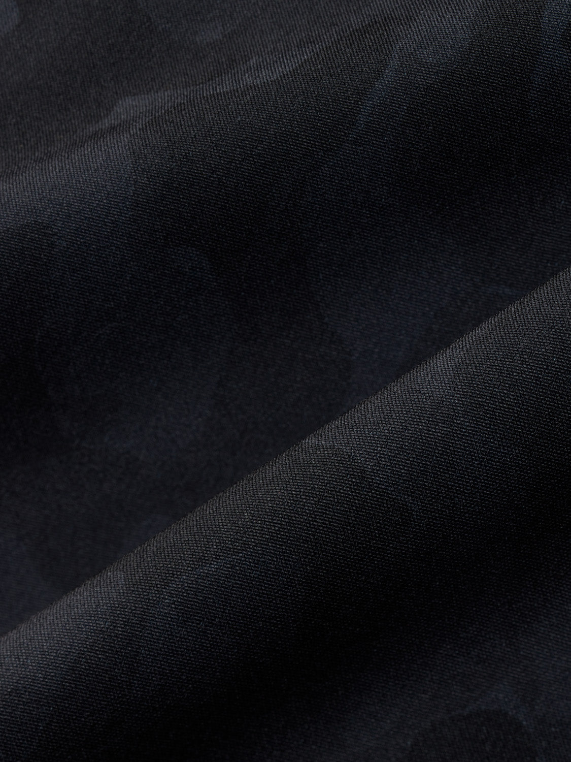 Black camo patterned fabric with textured weave showing folded material detail.