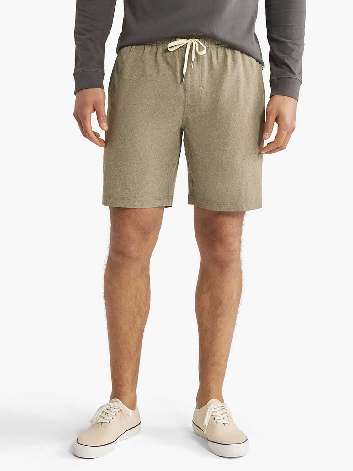 Man wearing olive green shorts with a drawstring waist and cream-colored canvas sneakers.