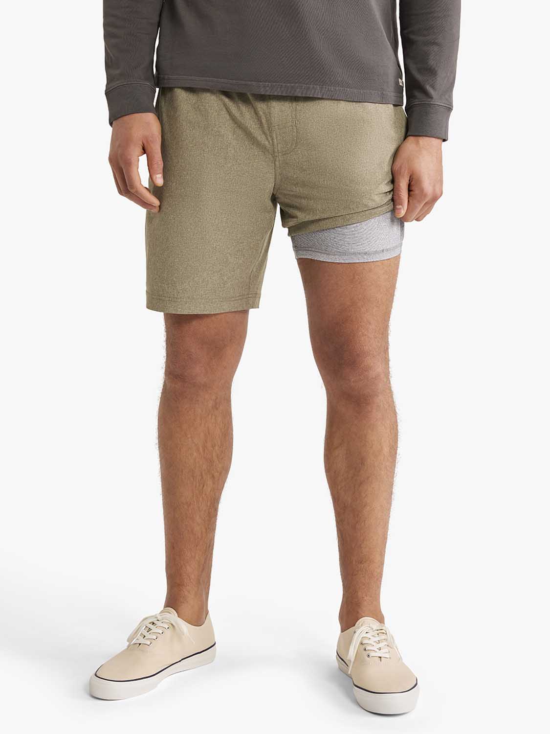 Man wearing olive-colored shorts with gray waistband detail and cream canvas sneakers.