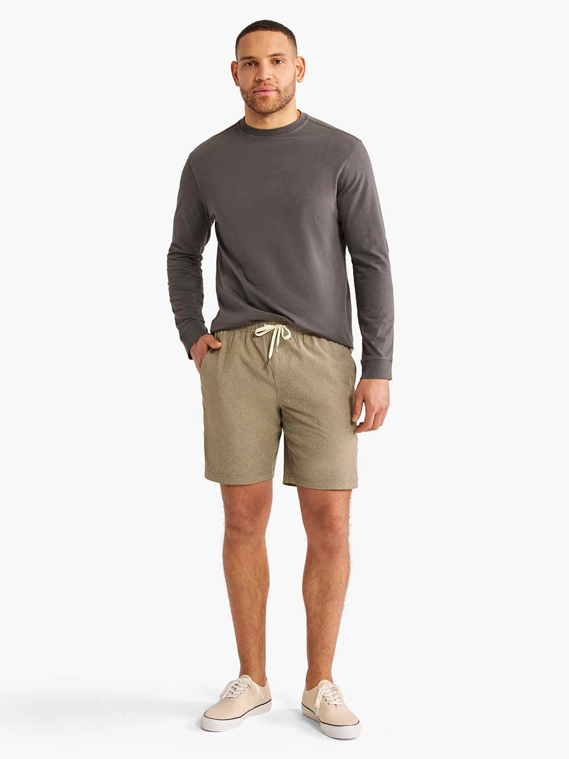 Man wearing charcoal long-sleeve shirt and olive drawstring shorts with canvas sneakers.